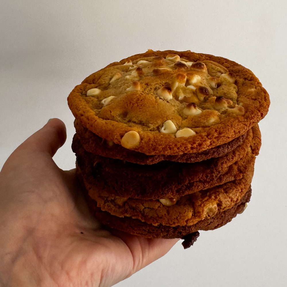 A hand holding a tall stack of freshly baked white chocolate chip cookies